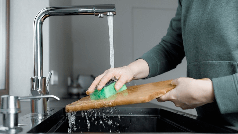 Person cleaning wood cutting board with sponge